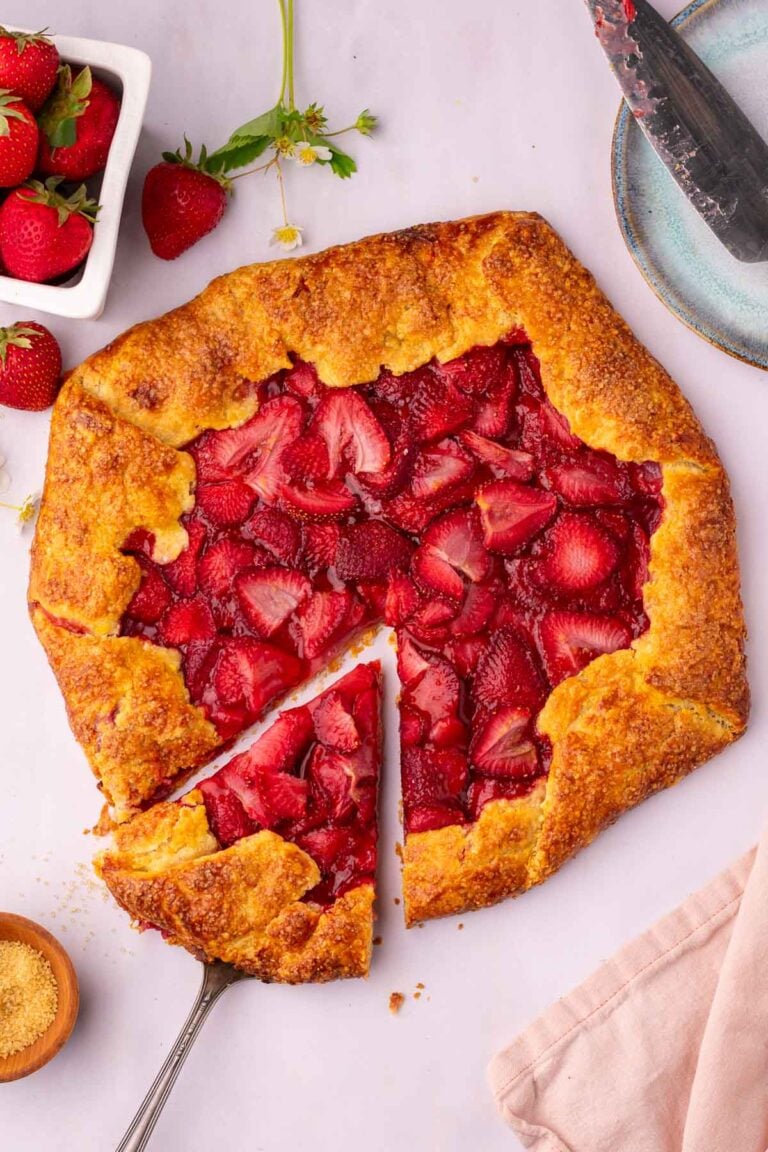Cutting out a slice of sourdough strawberry galette with a flaky sourdough galette crust and fresh strawberries around it.