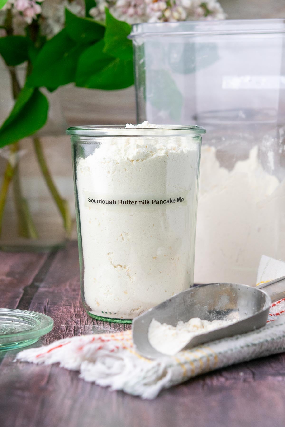 Homemade sourdough buttermilk pancake mix in a jar with a flour scoop beside it.
