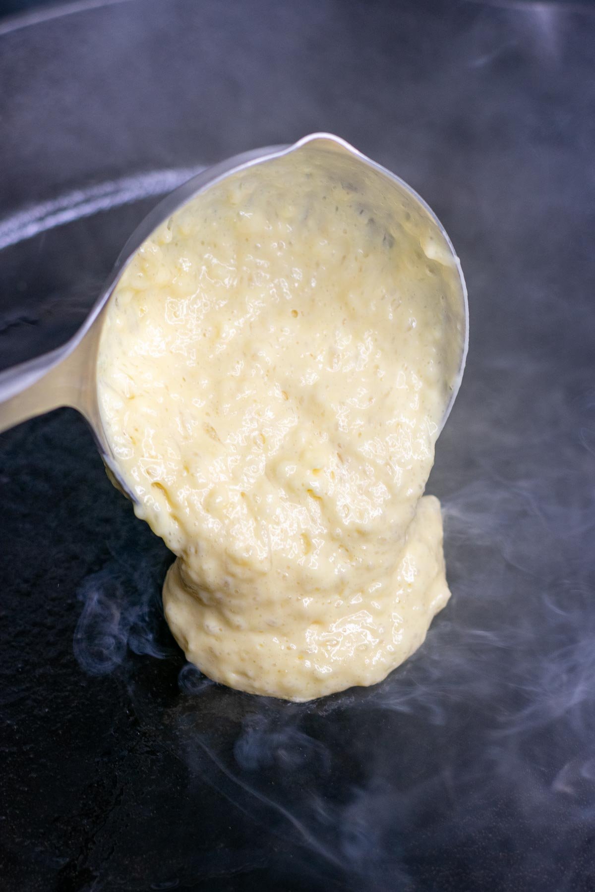 Ladling sourdough buttermilk pancake batter into a cast-iron skillet.