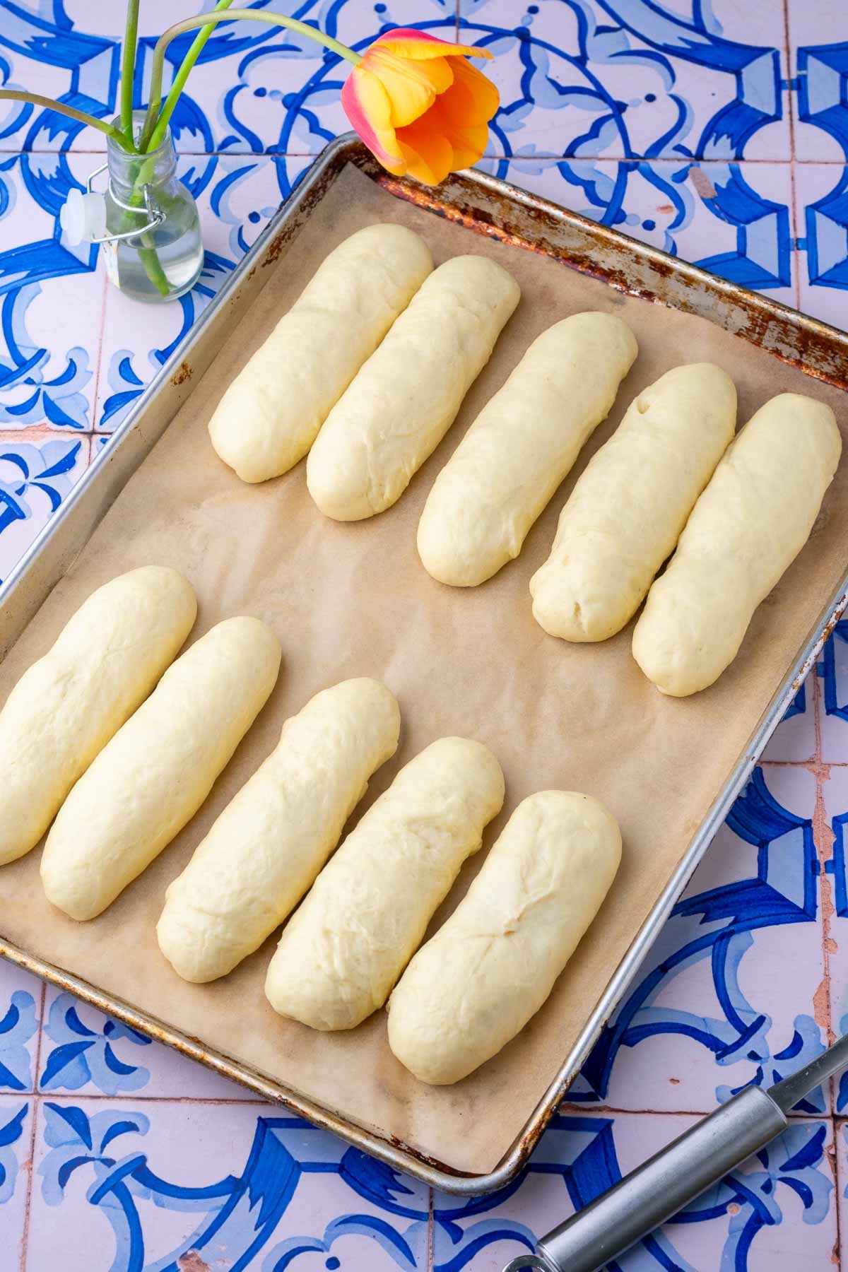 Ten sourdough hot dog buns doubled in size on a parchment lined baking sheet at the end of final proofing.