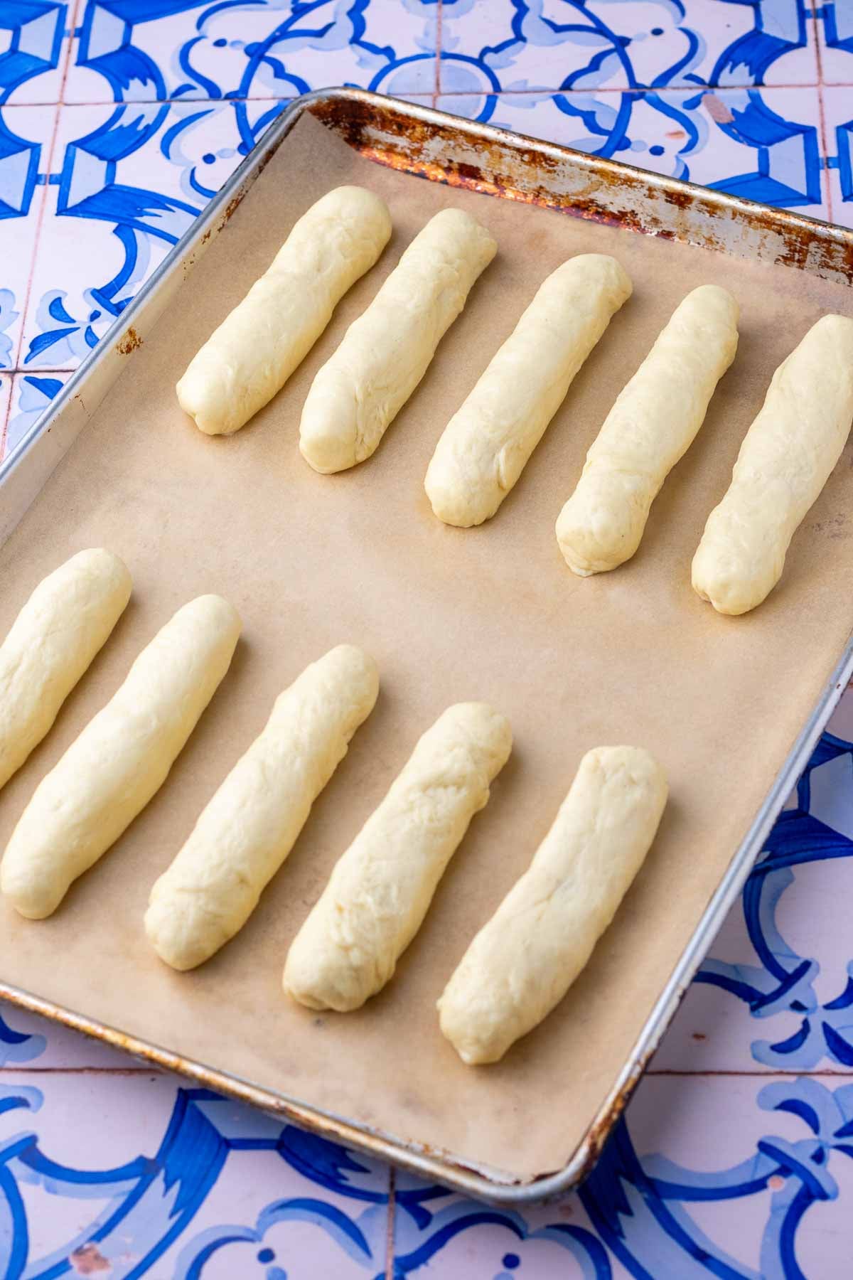 Sourdough hot dog buns on parchment lined baking sheet at the start of final proofing.