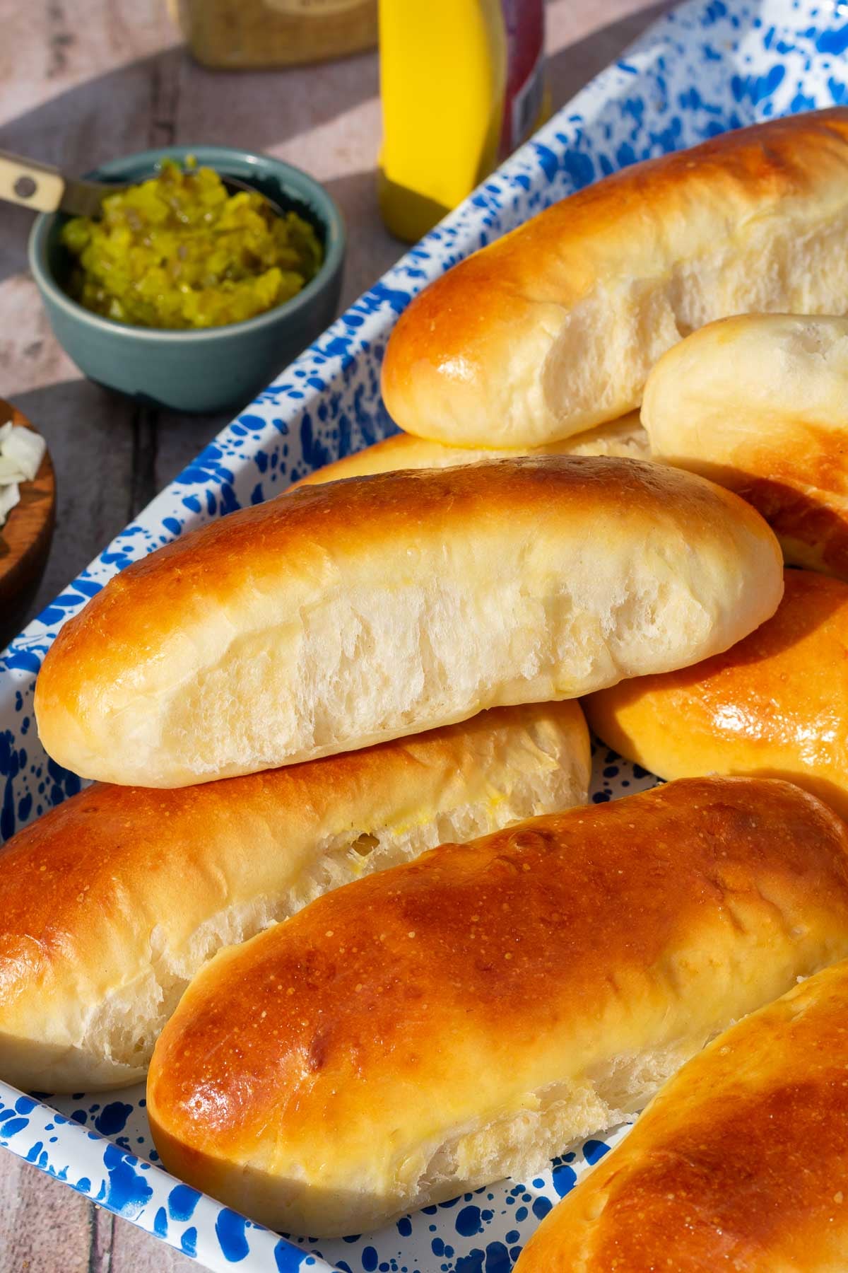 Soft sourdough hot dog buns on a platter with condiments in the background.