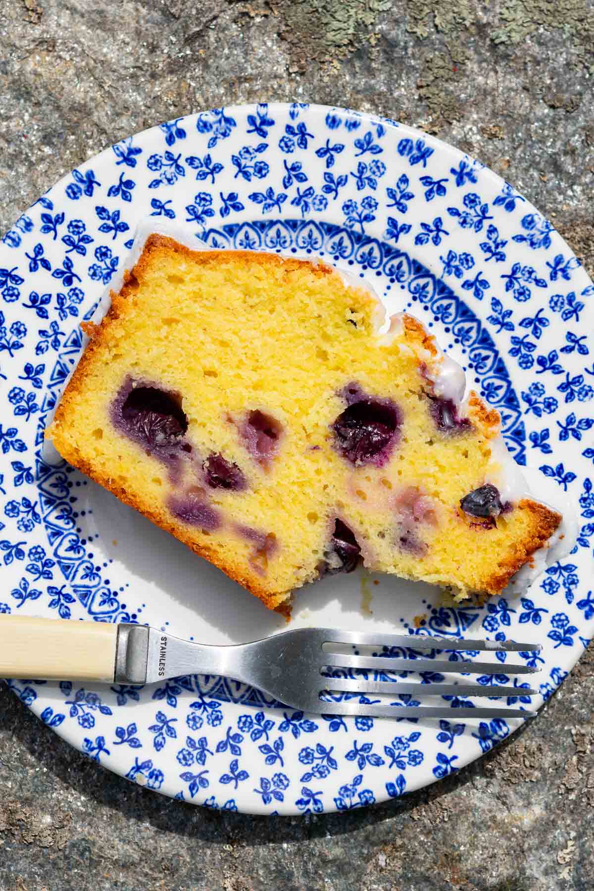 Slice of lemon blueberry sourdough pound cake on a plate with a fork and a bite taken out.