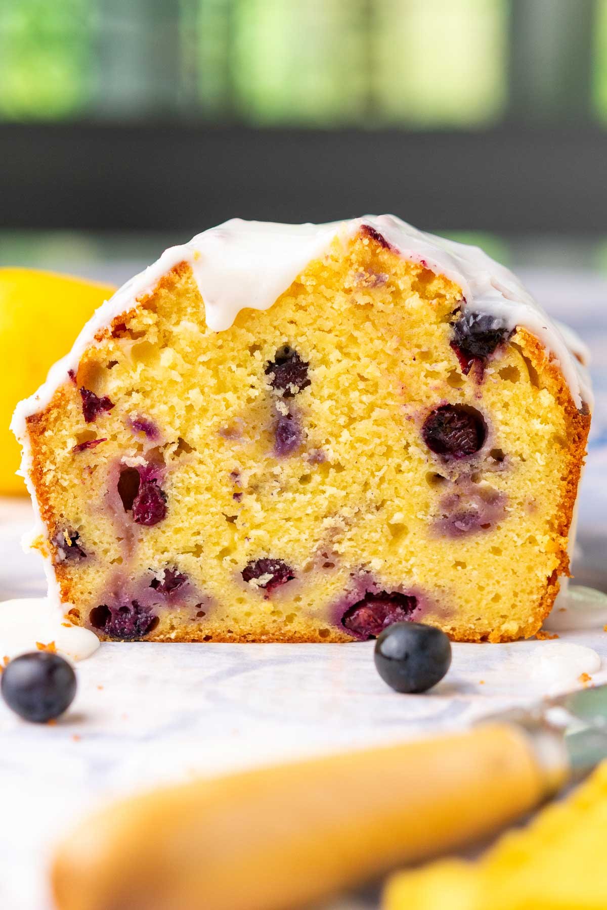 Tender crumb of lemon blueberry sourdough pound cake slice with fresh blueberries and lemon glaze.
