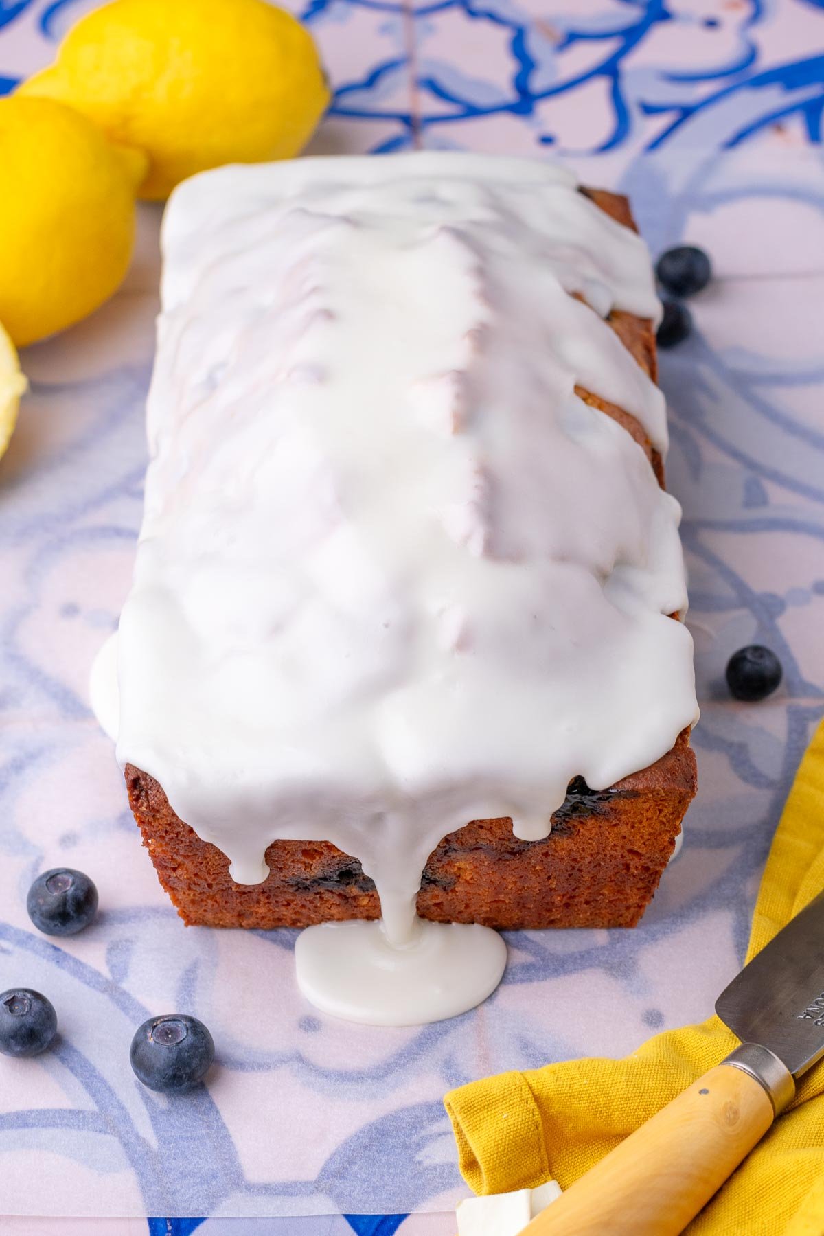 Glazed lemon blueberry sourdough pound cake with lemons and blueberries around it.