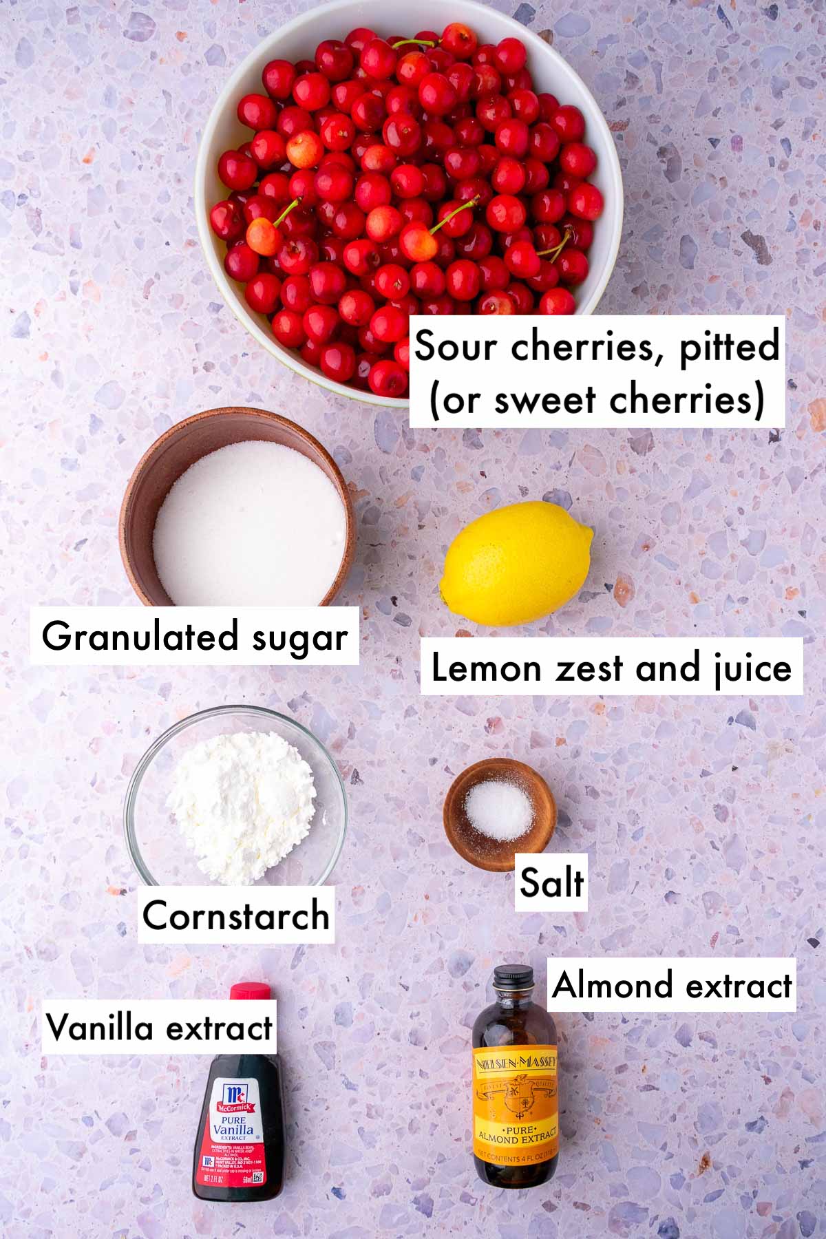 Labeled ingredients needed for sour cherry pie filling including sour cherries, sugar, lemon, salt, cornstarch, vanilla and almond extract.