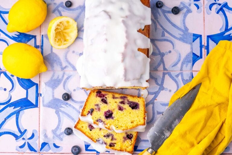 Sliced lemon blueberry sourdough pound cake with lemons and blueberries around it.