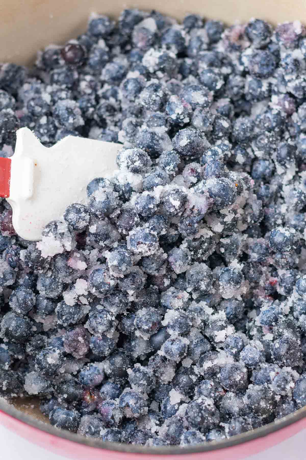Mixing blueberries and sugar in a Dutch oven with a spatula.