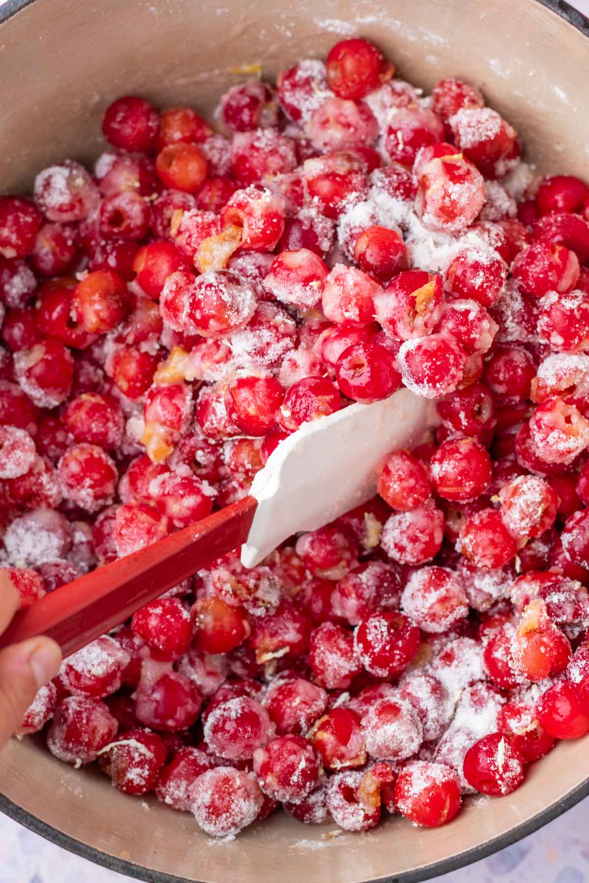 Mixing sour cherries in Dutch oven with spatula and sugar.