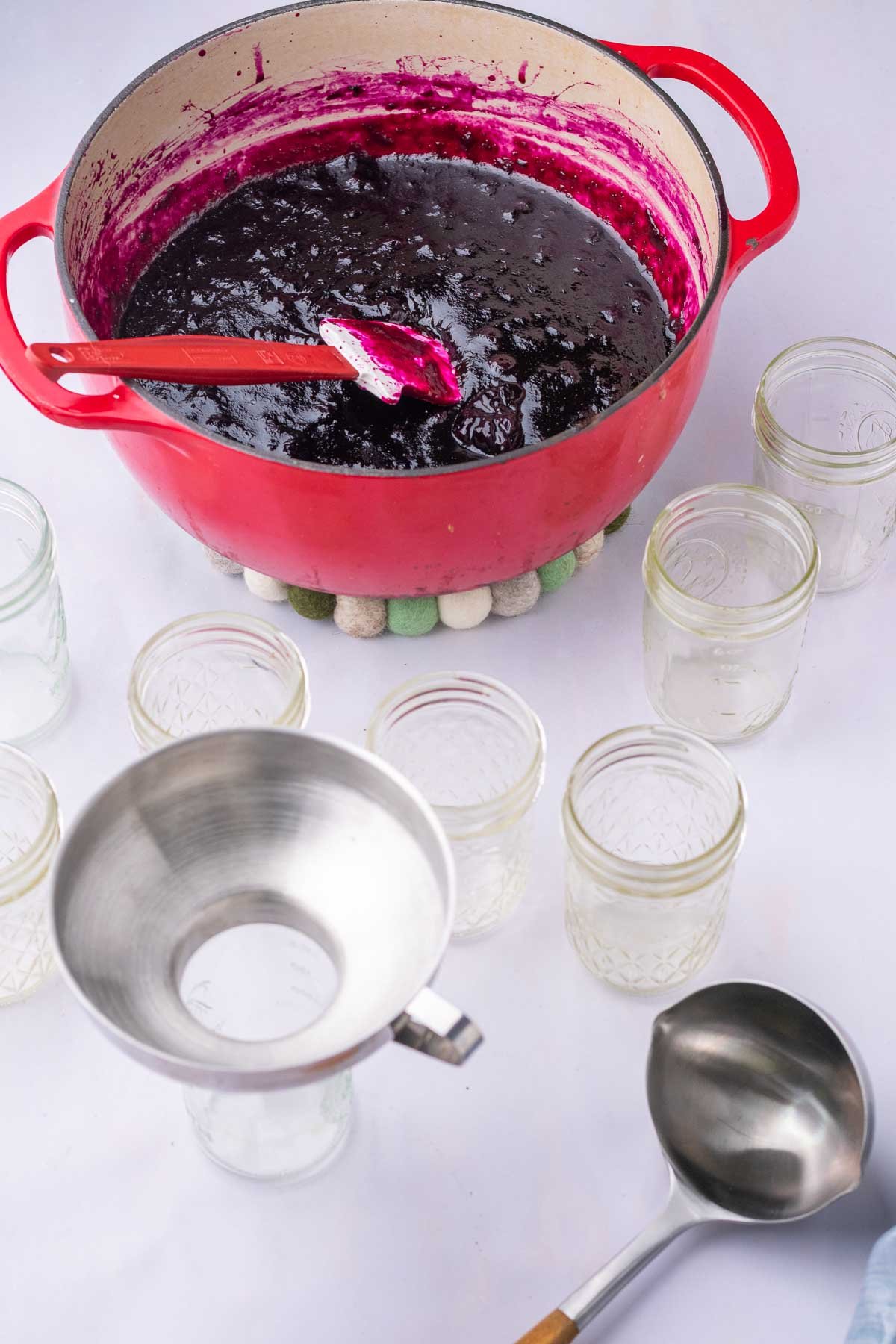 Canning setup for blueberry jam with a dutch oven full of blueberry jam, mason jars, funnel, and a ladle.