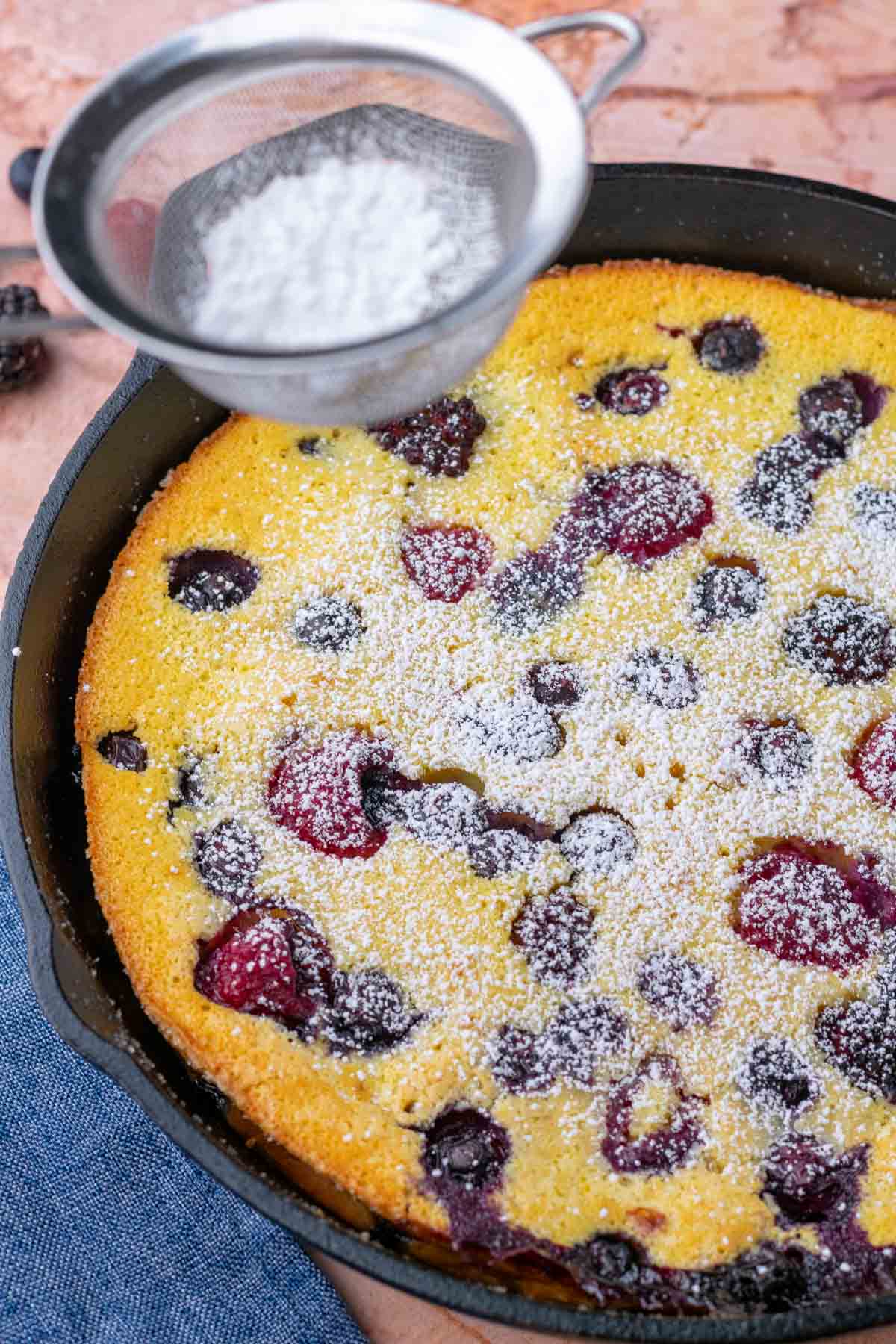 Dusting mixed berry sourdough clafoutis with powdered sugar.