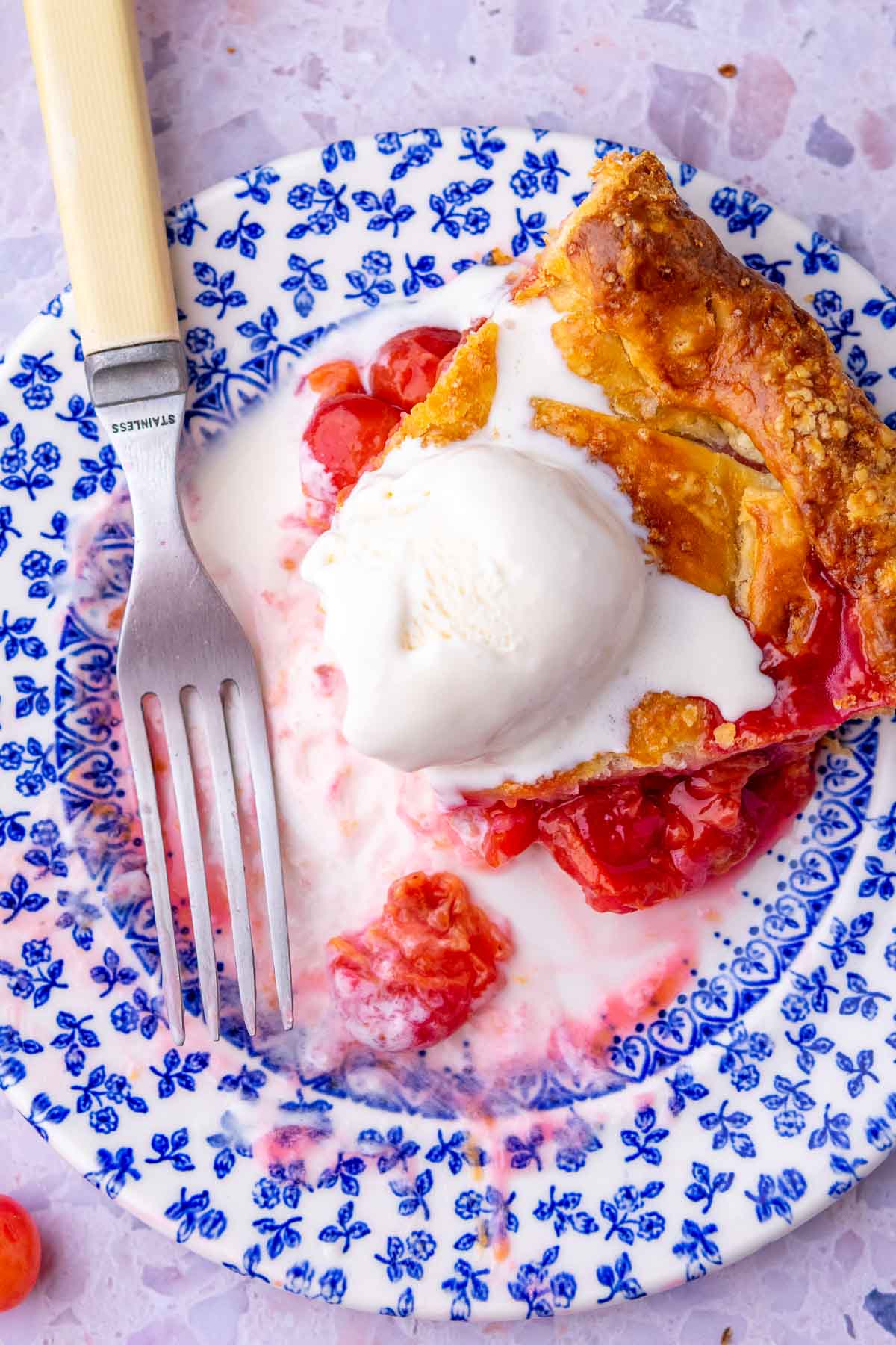 Bites taken out of a slice of sour cherry pie on a plate with a scoop of ice cream and a fork.