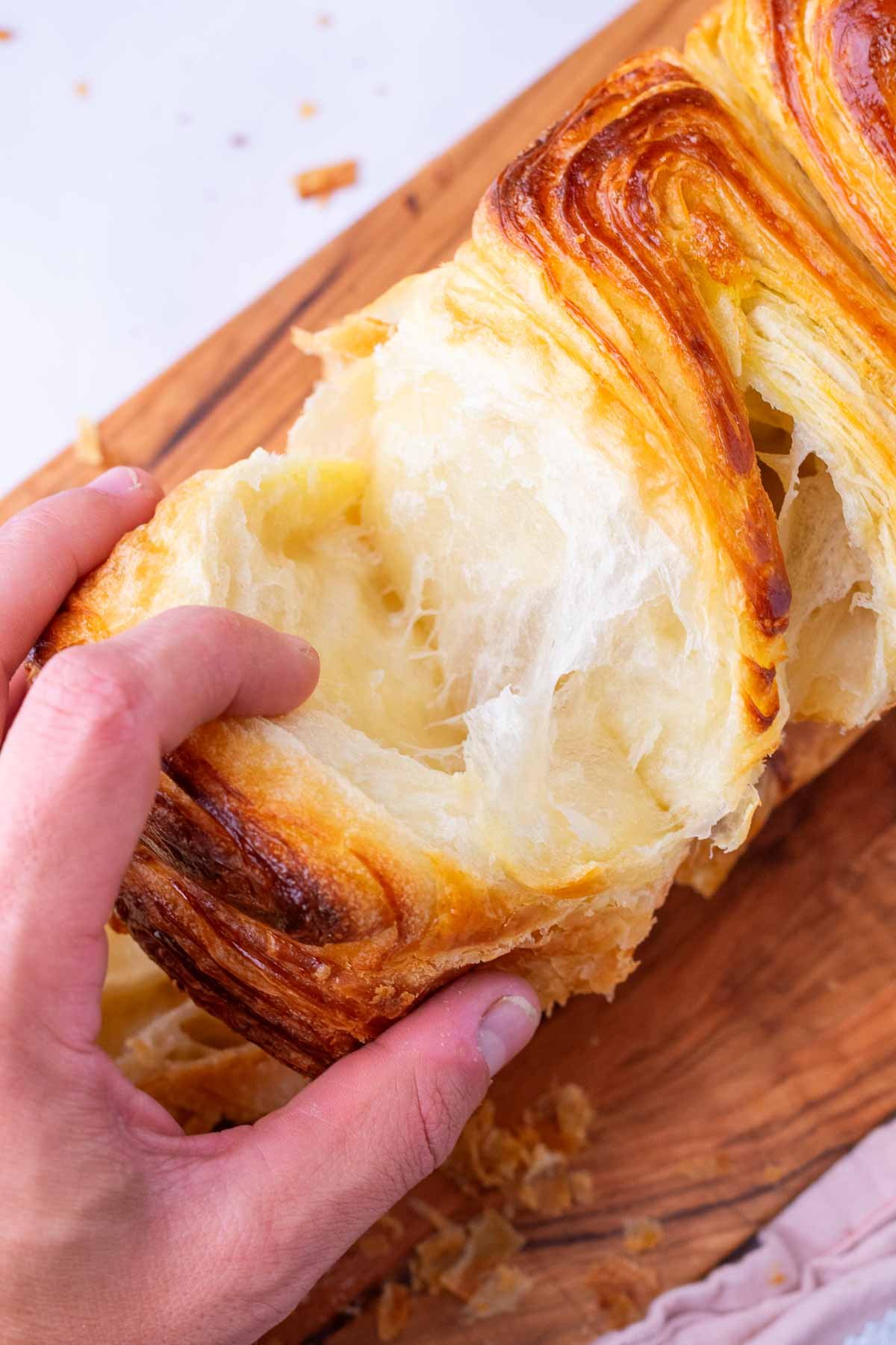 Hand pulling apart flaky and buttery layers of sourdough croissant bread loaf.