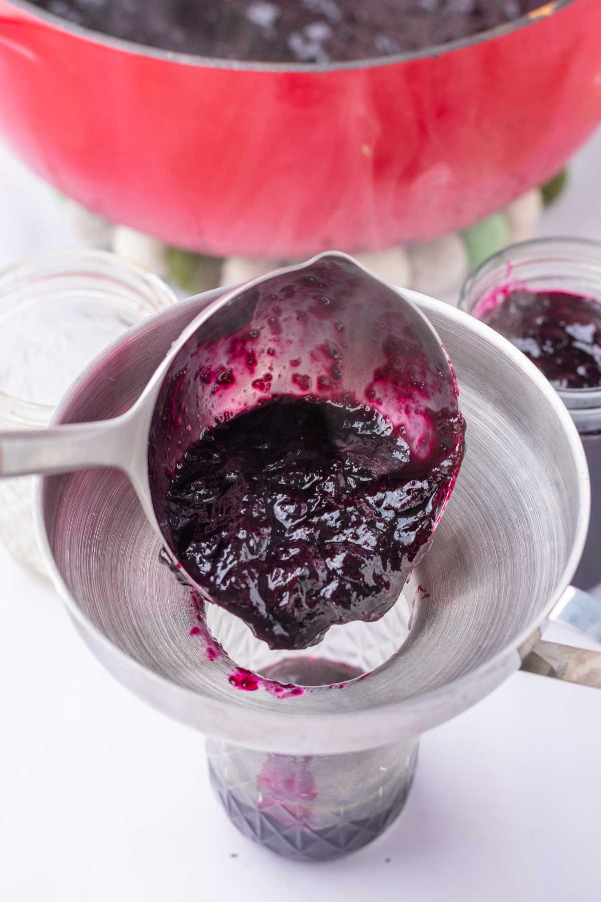 Pouring blueberry jam from a ladle into a mason jar with a funnel for canning.