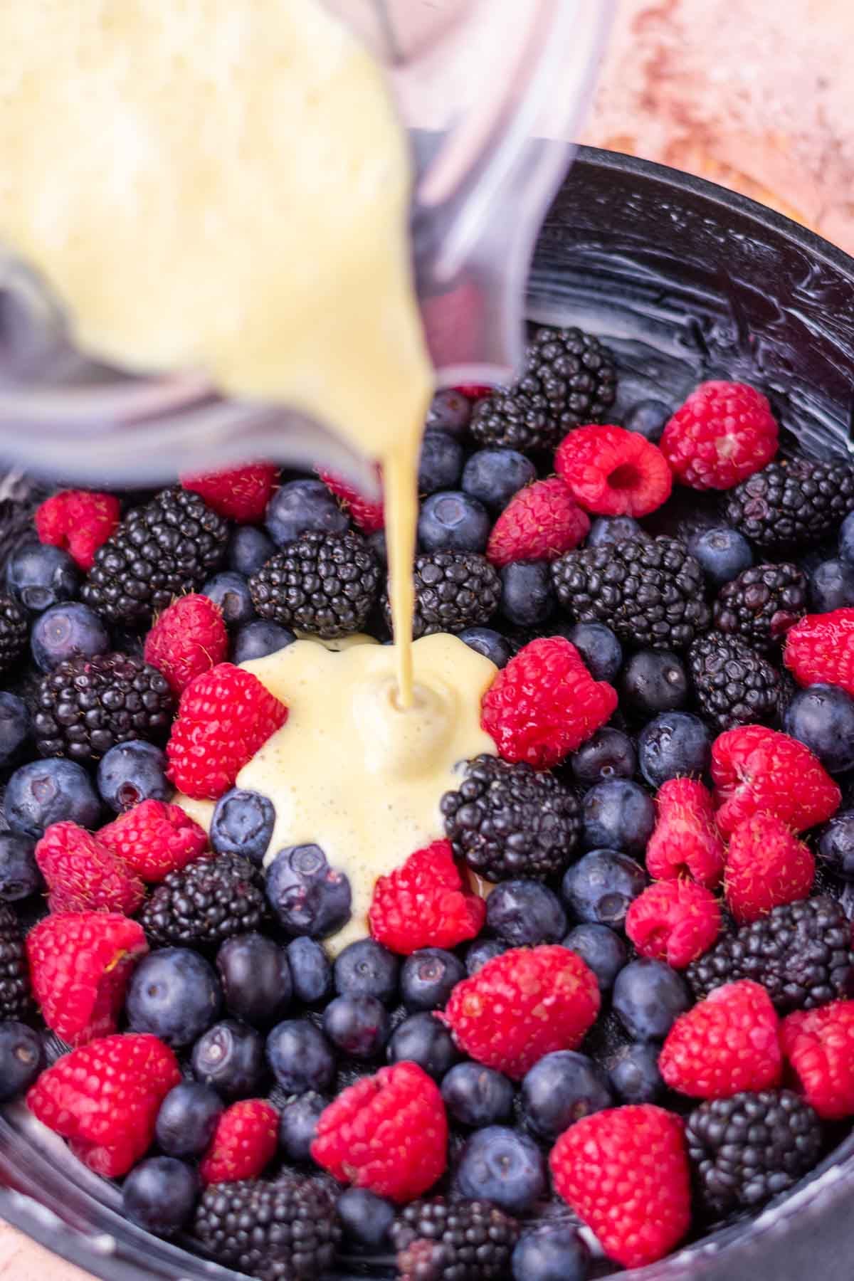 Pouring sourdough clafoutis batter from a blender into a cast-iron skillet with mixed berries.