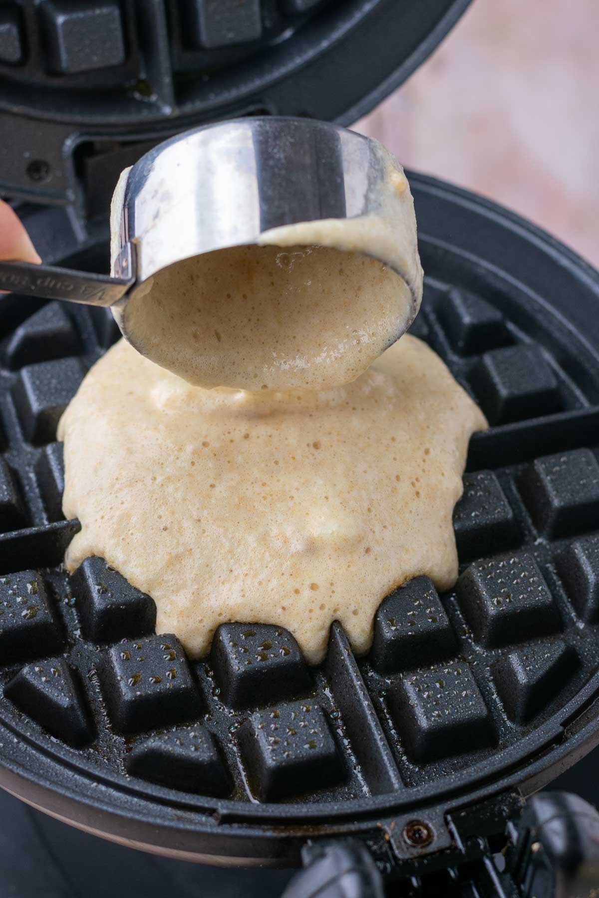Pouring sourdough einkorn waffle batter onto a waffle iron with a scoop.
