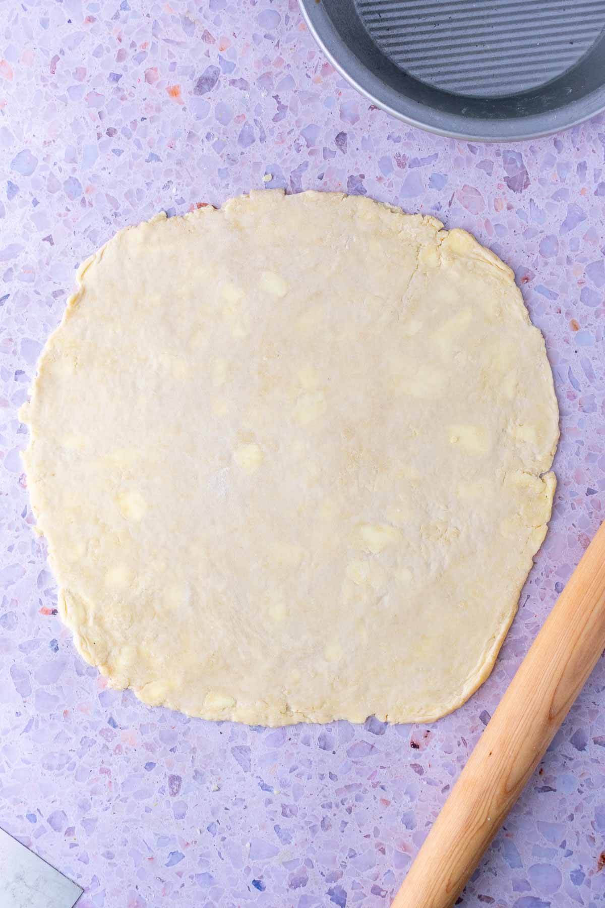 Rolled out sourdough pie crust in a large circle with a rolling pin.