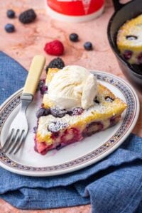 Slice of mixed berry sourdough clafoutis on a plate with a scoop of ice cream and a fork.