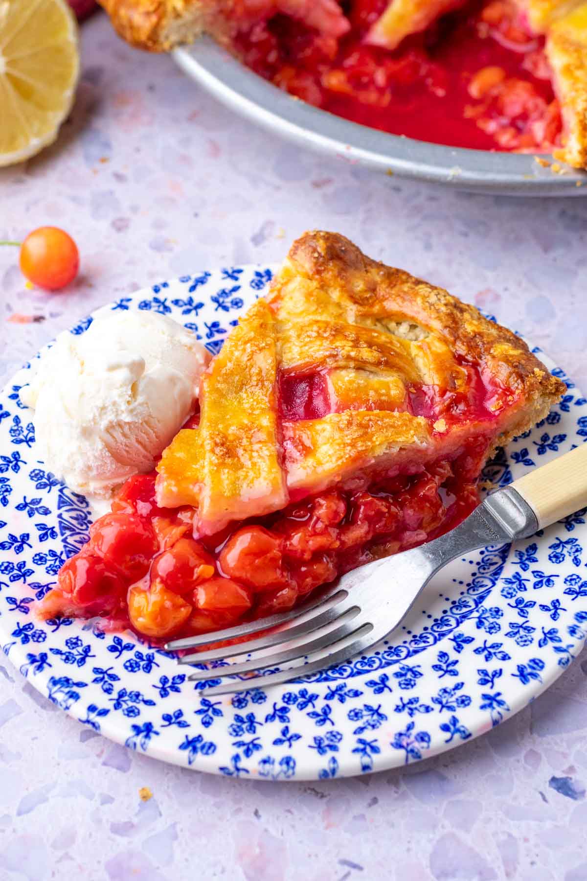 Slice of sourdough sour cherry pie on a plate with a scoop of ice cream and a fork.