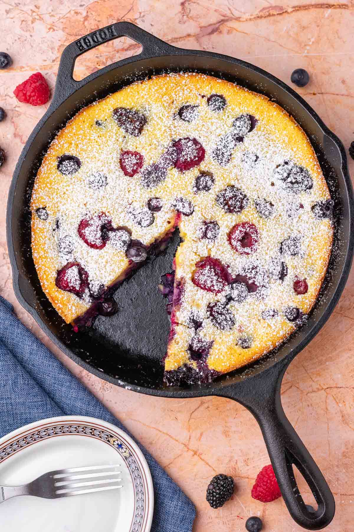 Slice taken out of mixed berry sourdough clafoutis in a cast-iron skillet.