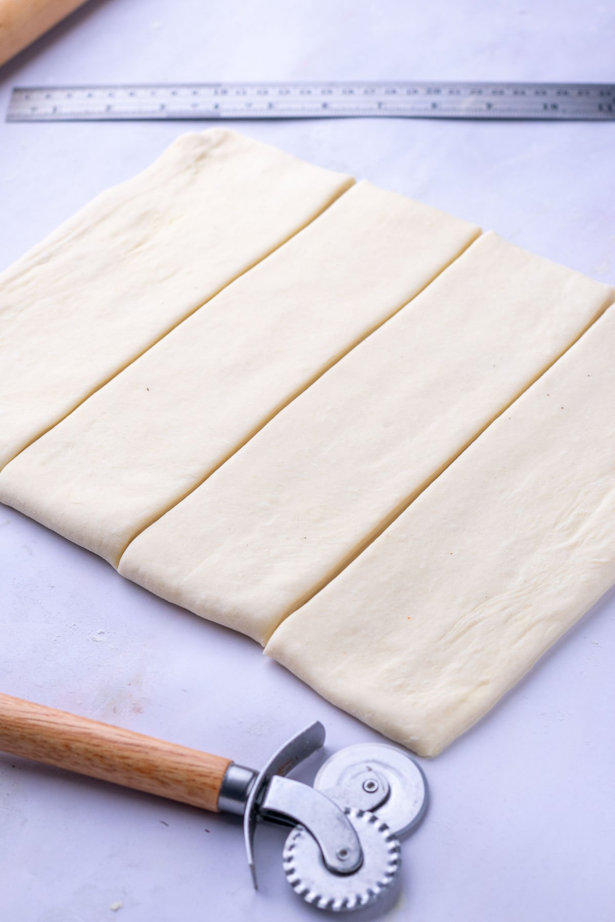 Four rectangular slices of sourdough croissant bread loaf dough with a ruler and pastry wheel.