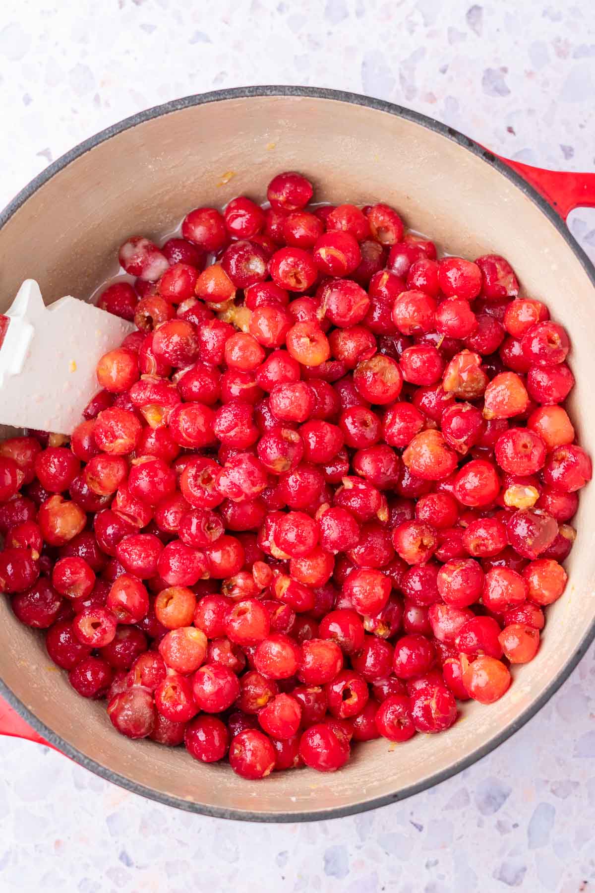 Start of cooking sour cherry filling in Dutch oven with spatula.