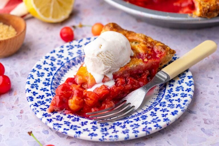 Slice of sour cherry pie made with sourdough pie crust and a scoop of ice cream with a fork on a plate.