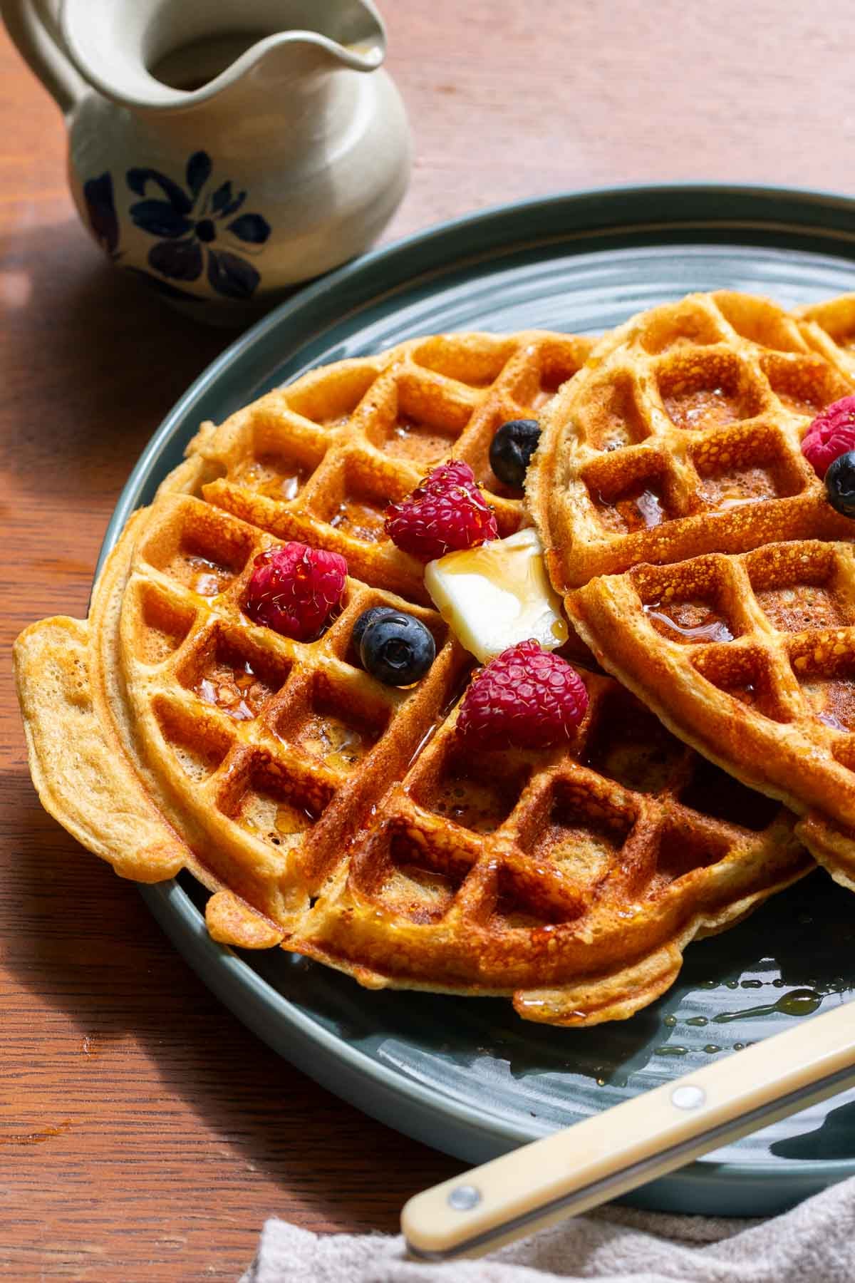 Plate with two sourdough einkorn waffles with berries, butter, and maple syrup.
