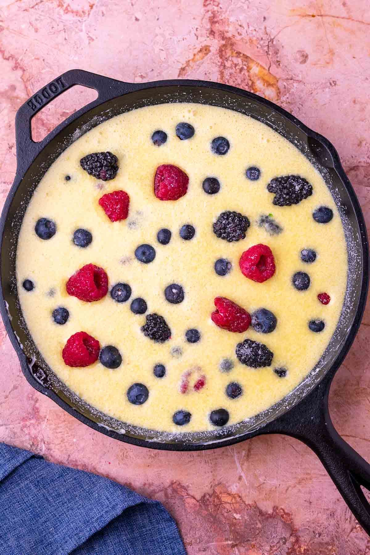 Unbaked mixed berry sourdough clafoutis in a cast-iron skillet.