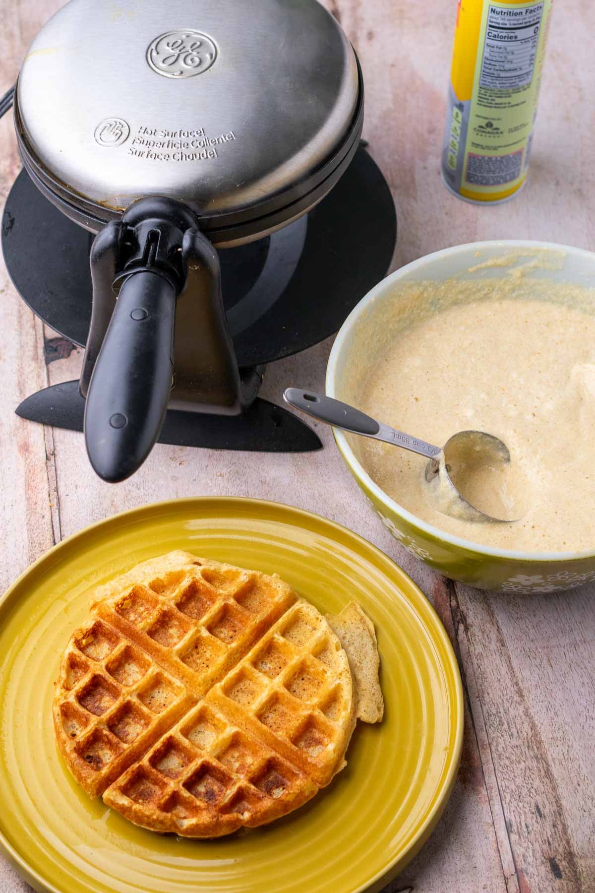 Waffle iron, sourdough einkorn waffle batter in a bowl, and a plate with a cooked waffle.
