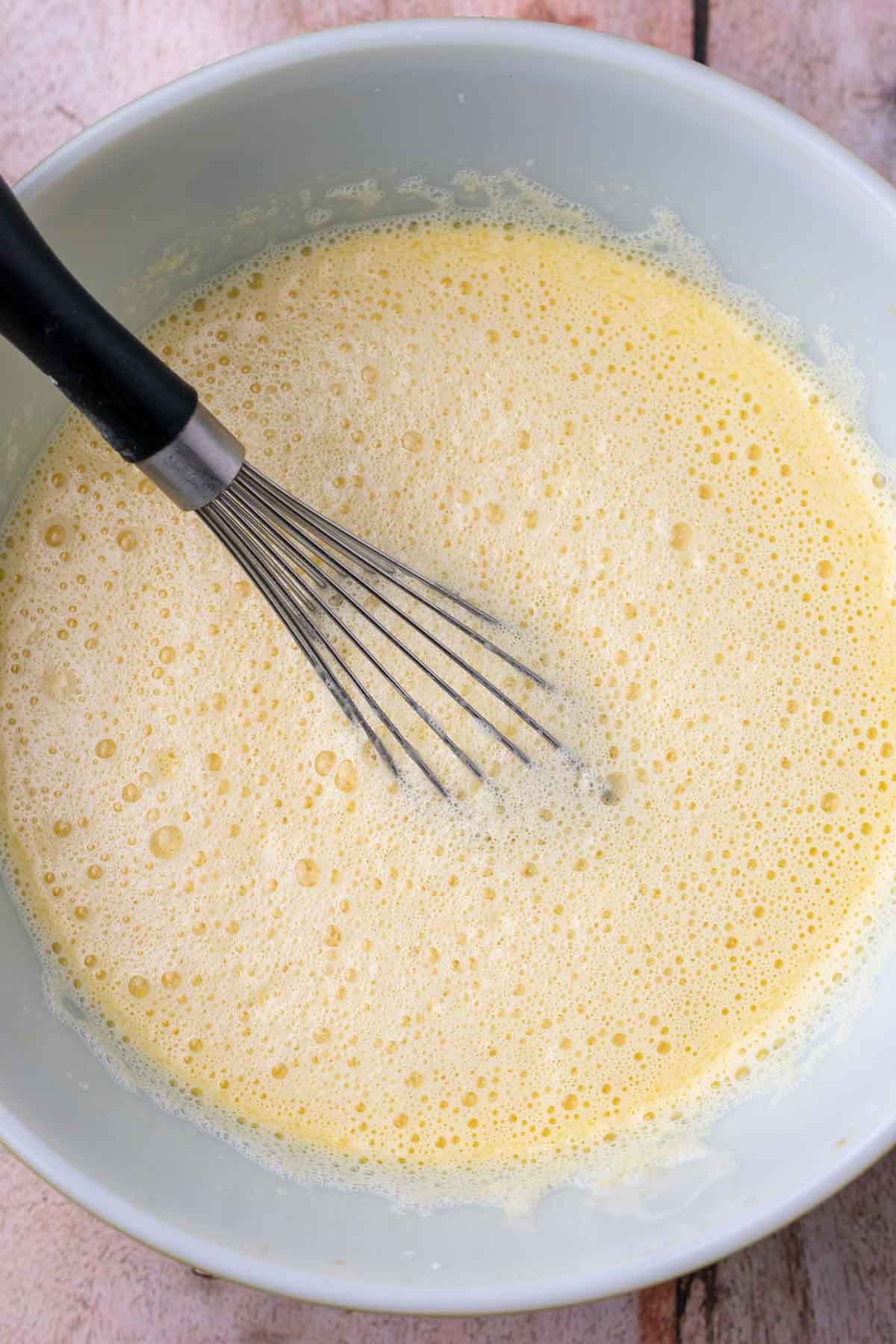 Bowl of mixed wet ingredients for sourdough einkorn waffles with a whisk.