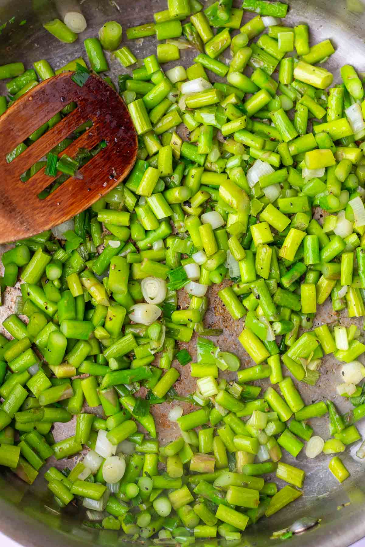 Cooking asparagus for sourdough quiche in a pan with a wooden spoon.