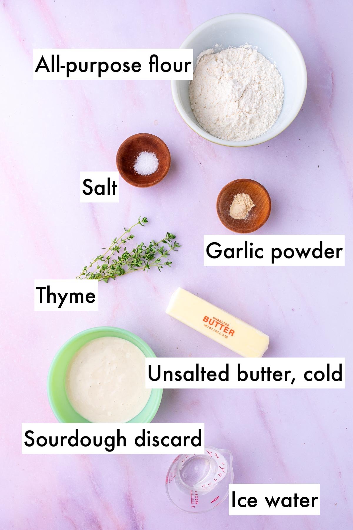 Labeled bowls of ingredients needed for savory sourdough pie crust including all-purpose flour, salt, garlic powder, thyme, unsalted butter, sourdough discard, and ice water.