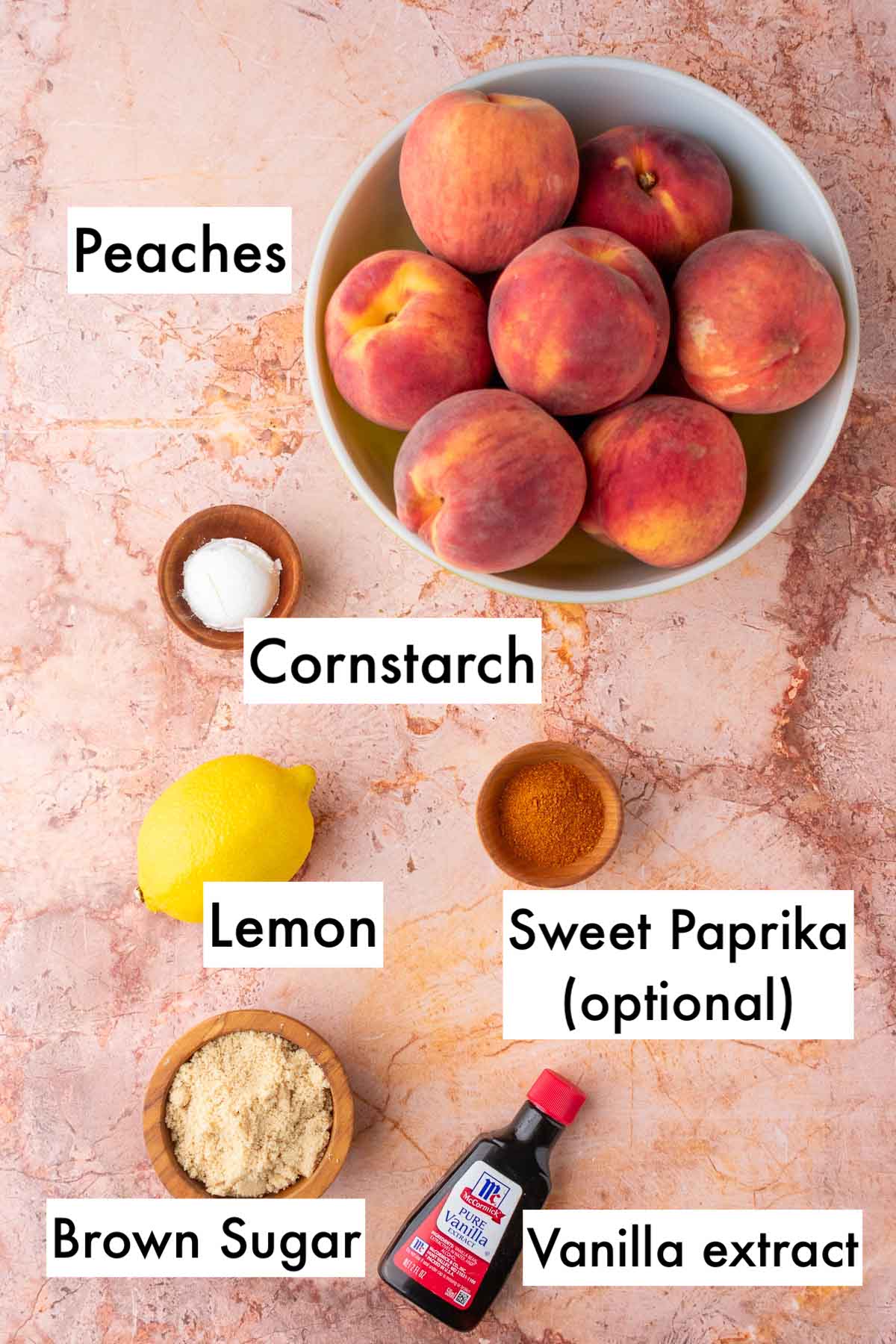 Labeled ingredients needed for sourdough peach cobbler filling including peaches, cornstarch, lemon, paprika, brown sugar, and vanilla.