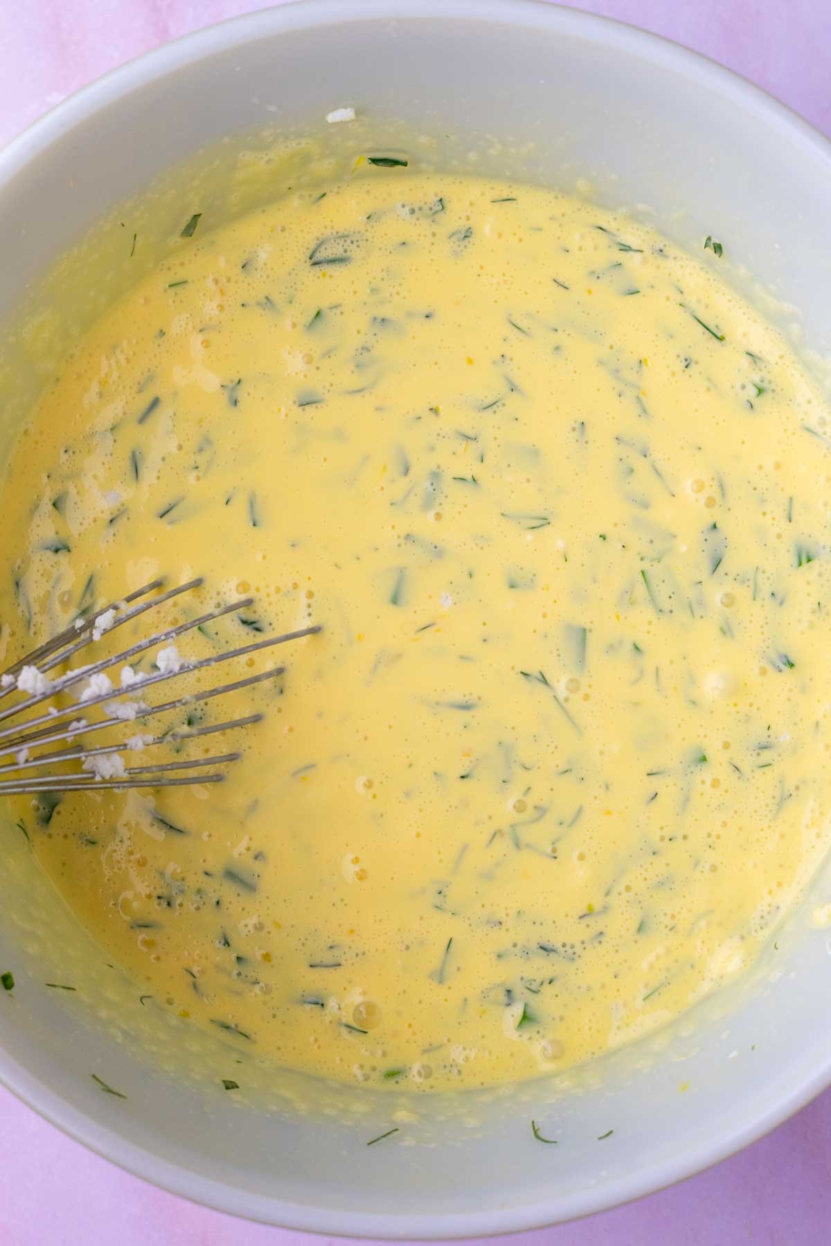 Mixing sourdough quiche ingredients in a bowl with a whisk.