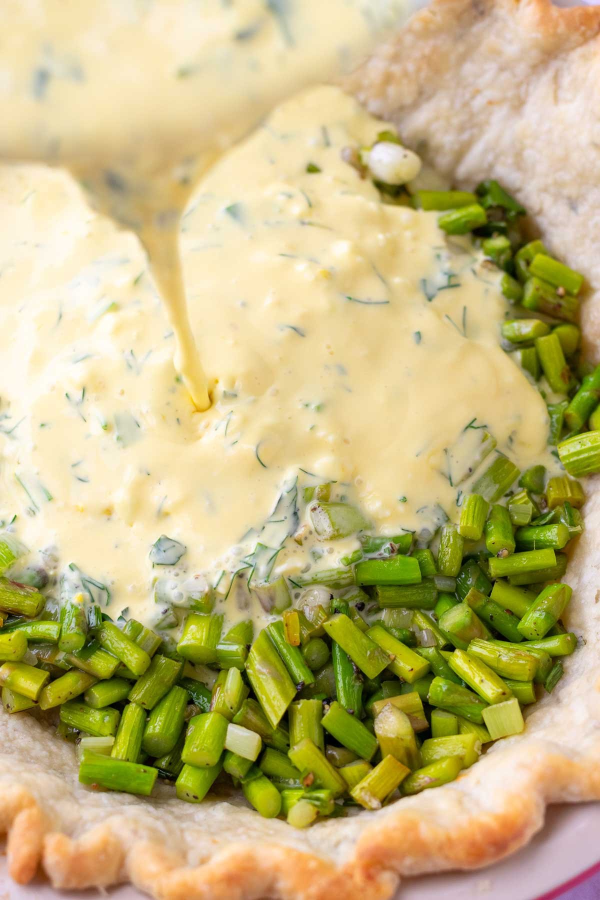 Pouring quiche mixture over asparagus in a sourdough pie crust.
