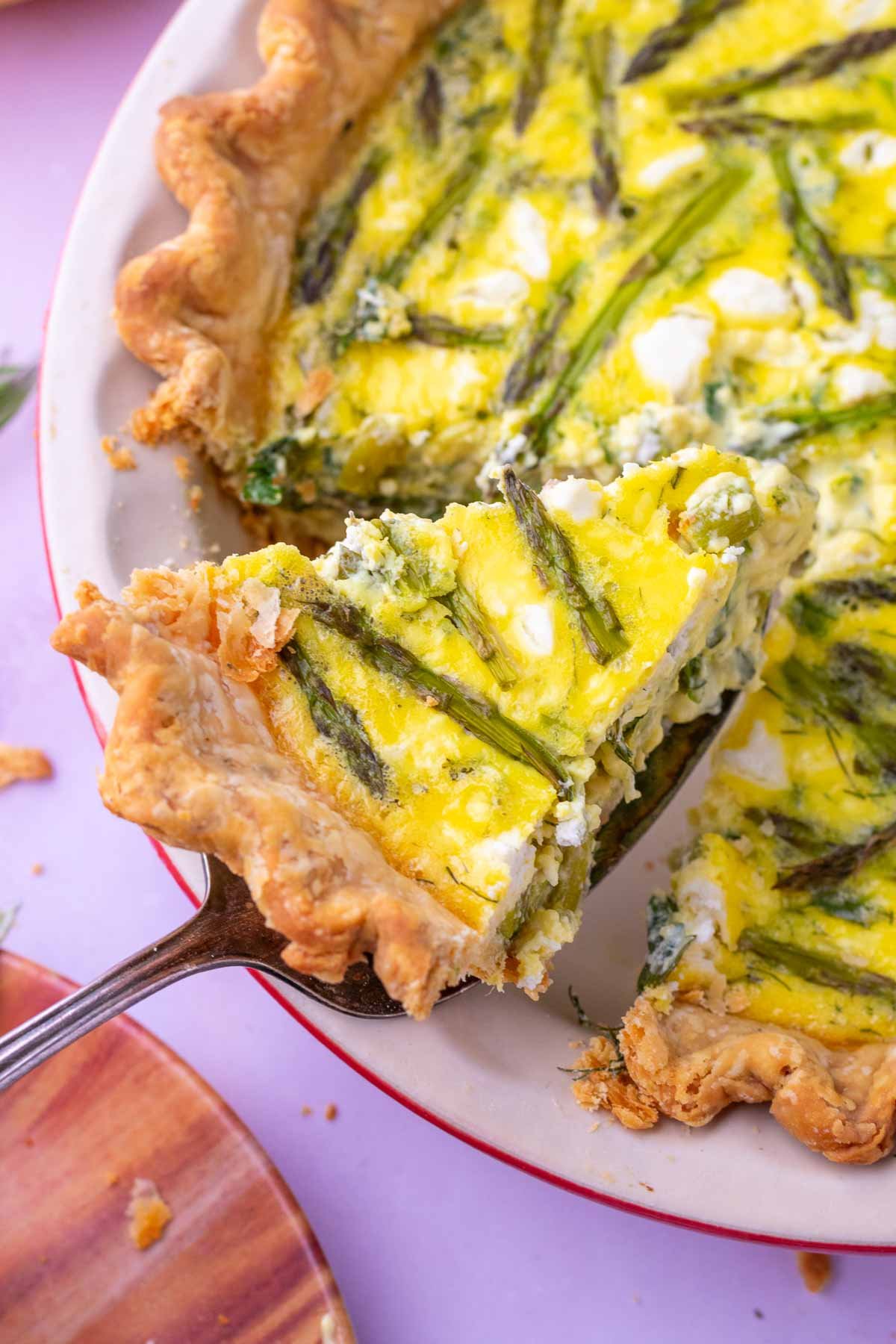 Cutting out a slice of asparagus goat cheese sourdough quiche from a pie plate.