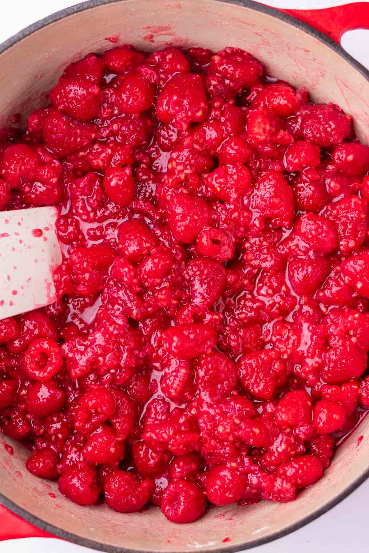 Start of cooking raspberry jam in a Dutch oven with a spatula.