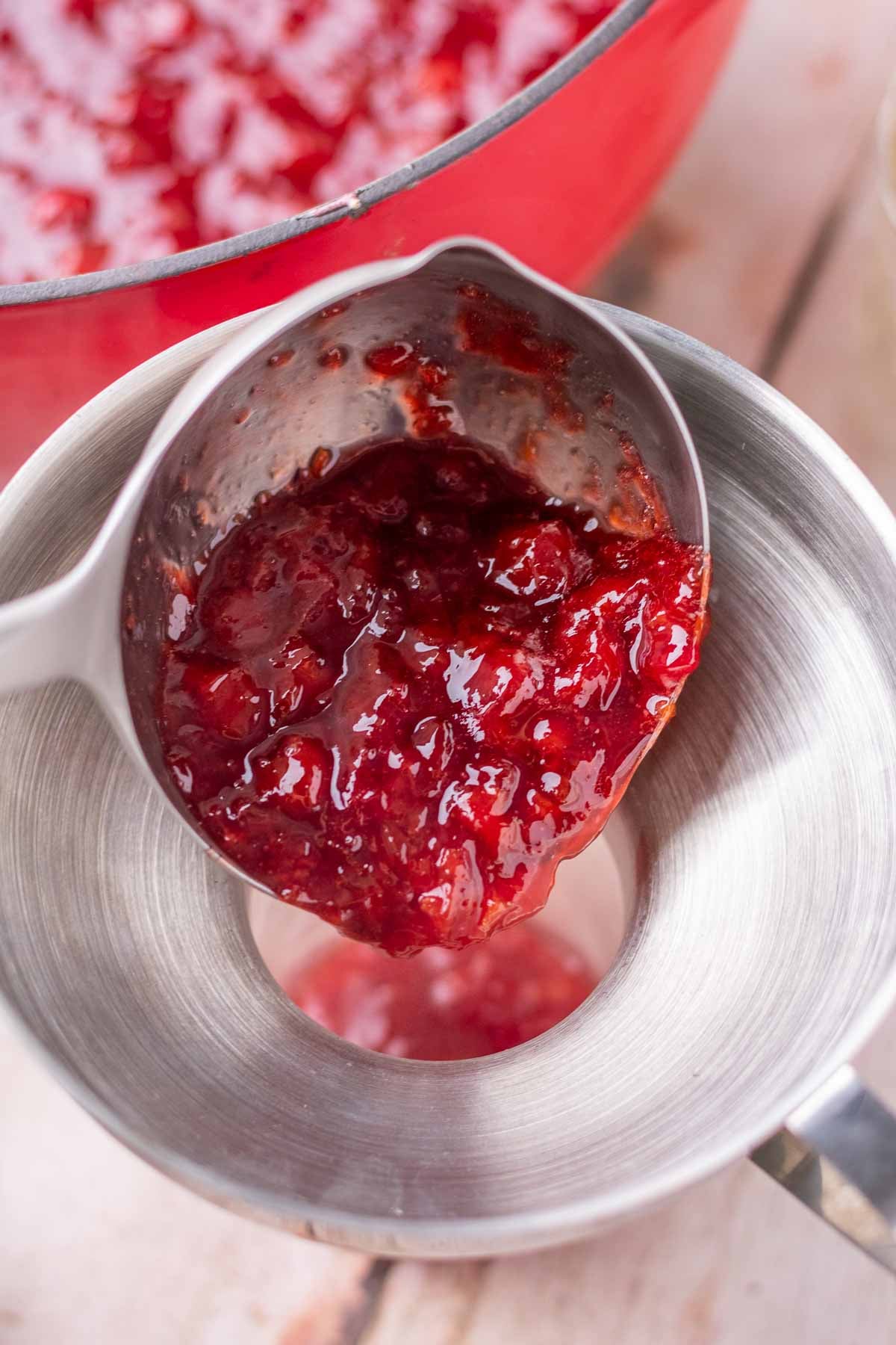 Ladling sour cherry jam into a mason jar for canning.