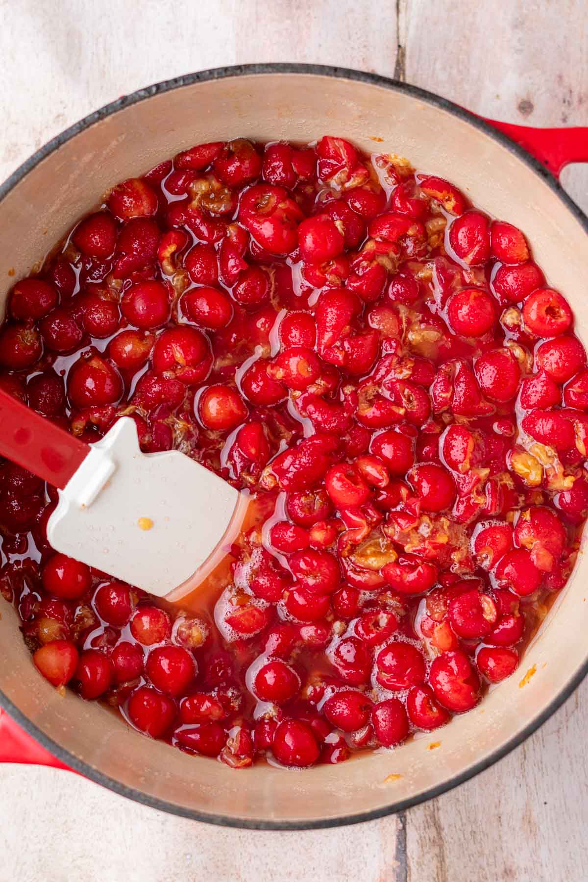Cooking sour cherry jam in a Dutch oven with a spatula.