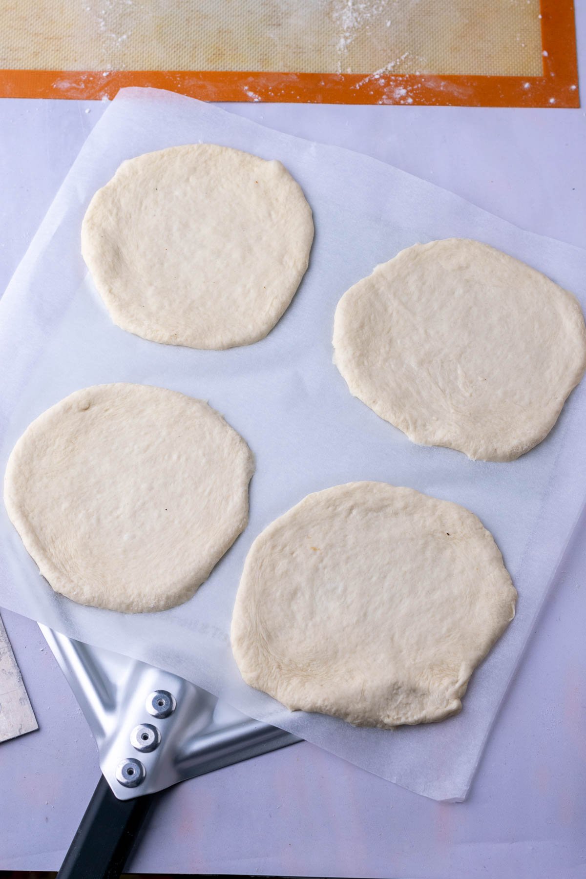 Four thin sourdough pita breads on a bread peel before baking.