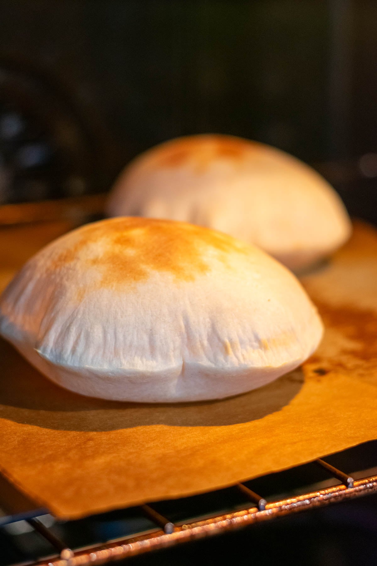 Two sourdough pita breads on bread steel in the oven puffing up.