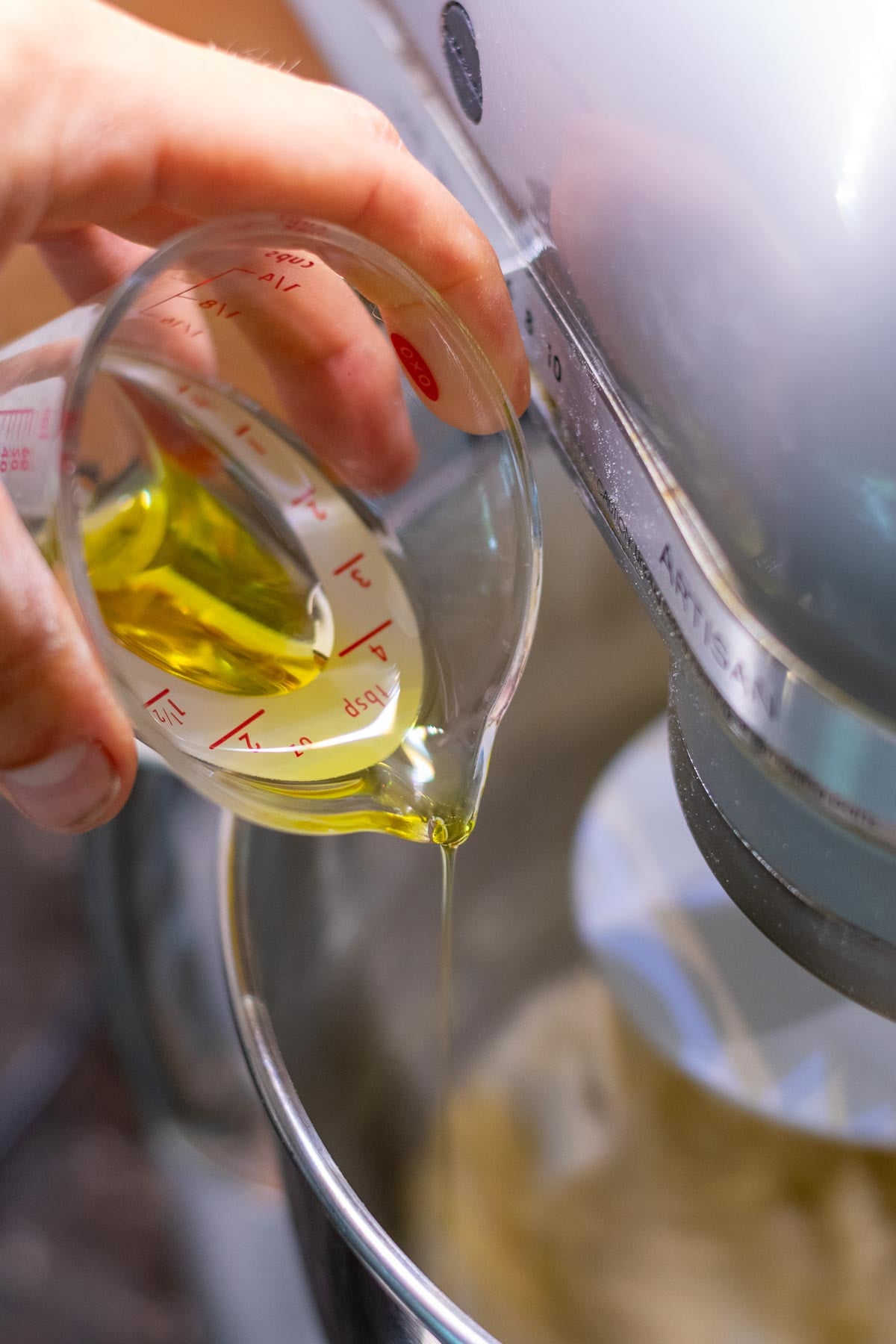 Pouring olive oil into sourdough pita bread dough in stand mixer.