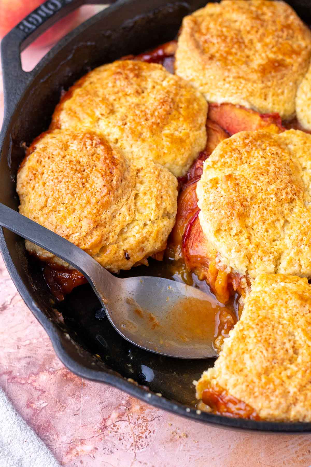 Serving sourdough peach cobbler in a cast-iron skillet with a large spoon.