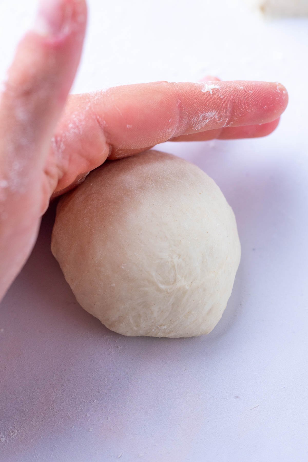 Hand rolling sourdough pita bread to shape into a round.
