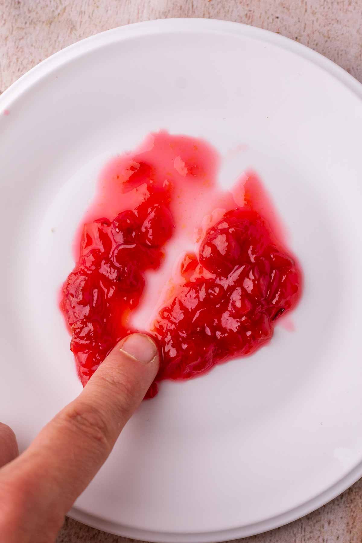 Finger running through sour cherry jam on a plate and it does not pass the finger plate test.
