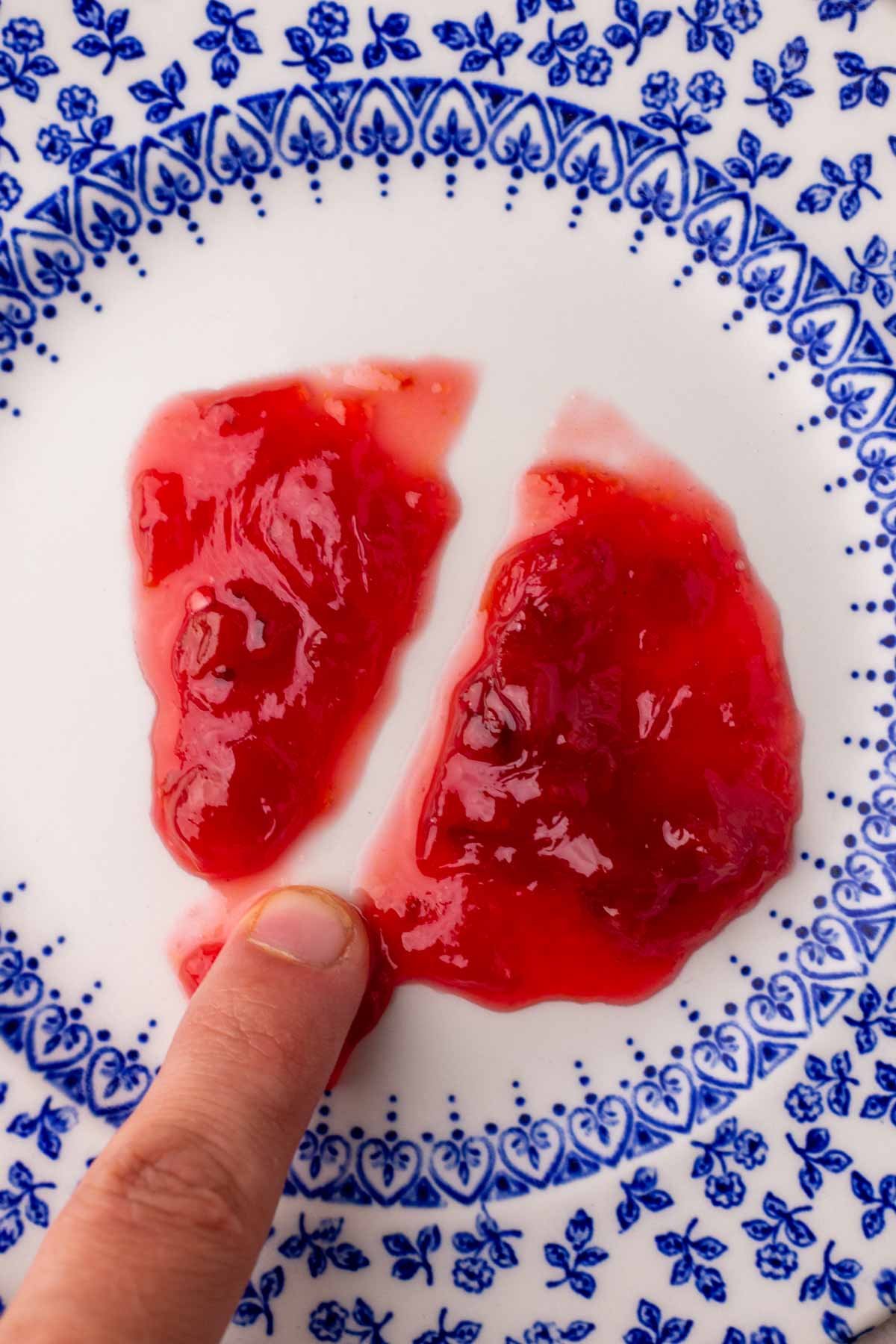 Sour cherry jam passes the finger plate test with a finger running through the center of the jam on a plate.