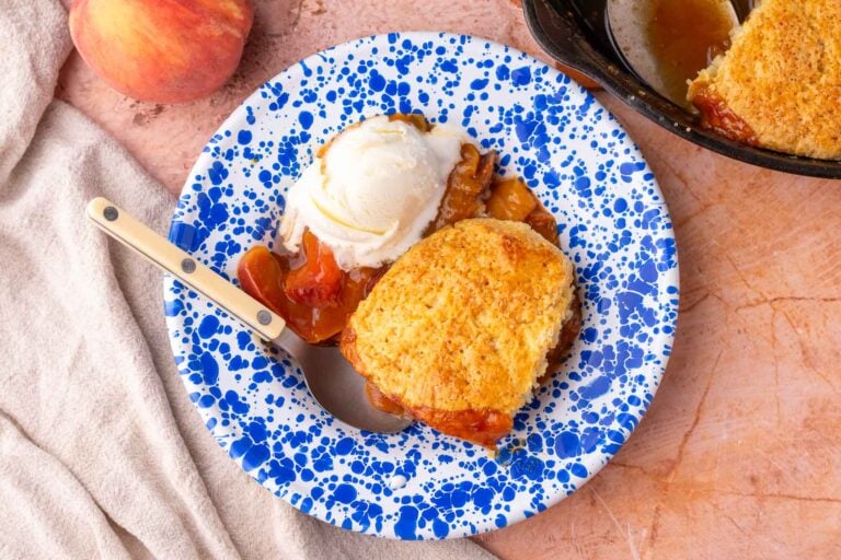 Sourdough peach cobbler with sourdough biscuit topping and ice cream in a bowl with a spoon.