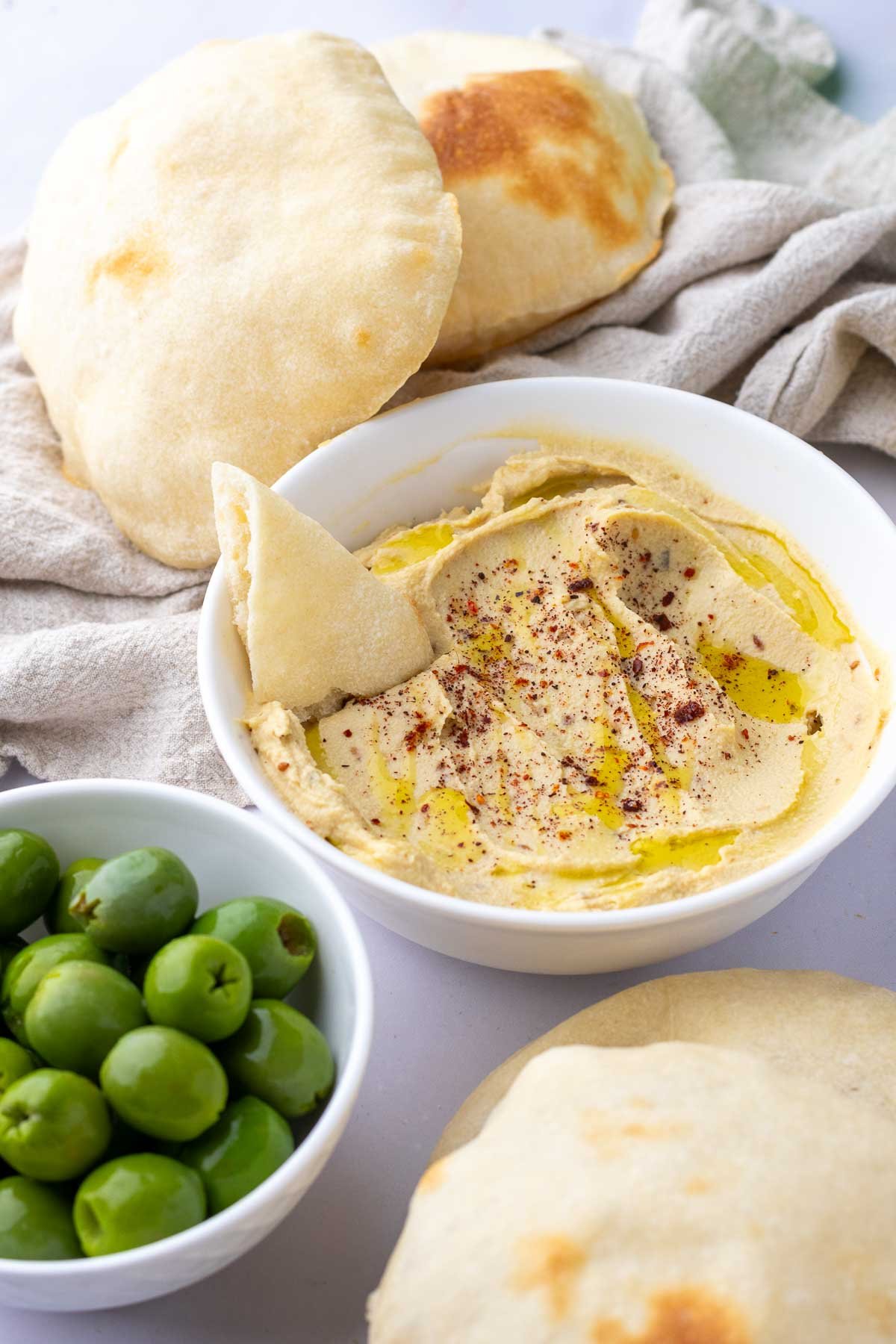 Sourdough pita bread dipped in hummus with a bowl of olives.