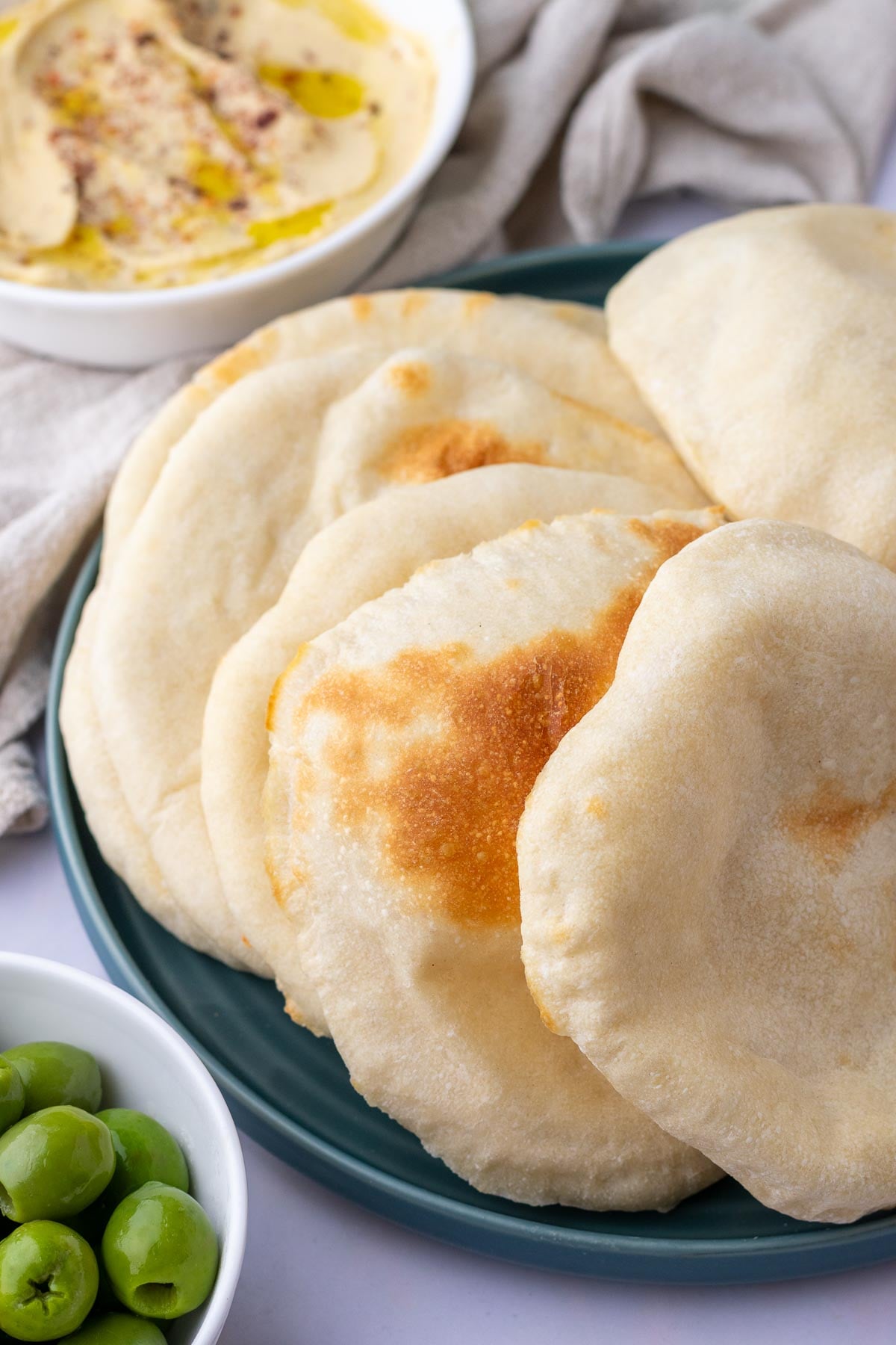 Sourdough pita breads on a plate with olives and hummus in the background.